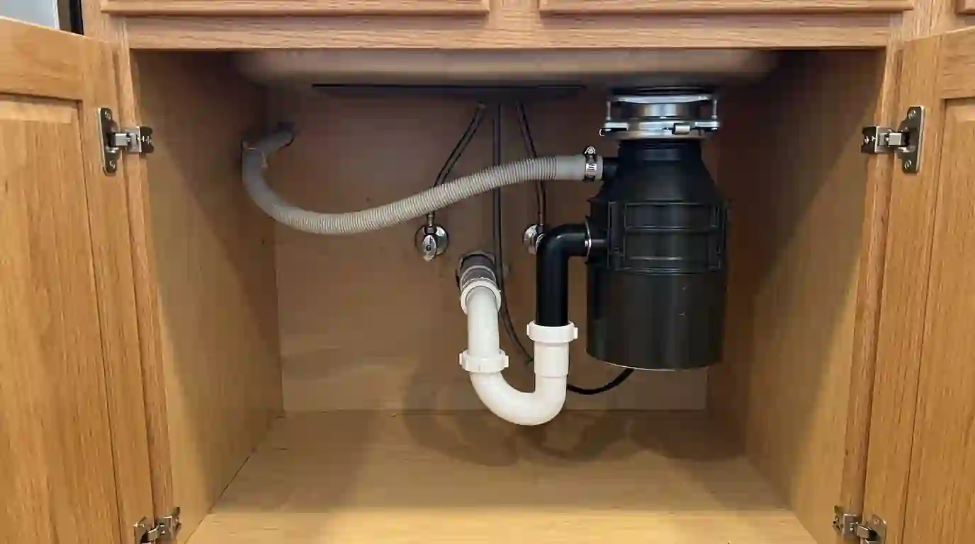 Under sink view of a new P trap and disposal with dishwasher hose connected